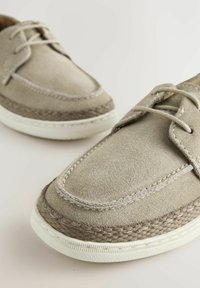 Szare zamszowe buty typu lace-up z haftowanym wzorem, biała gumowa podeszwa i pleciony detal na krawędzi. Teksturowana powierzchnia i subtelne akcenty.