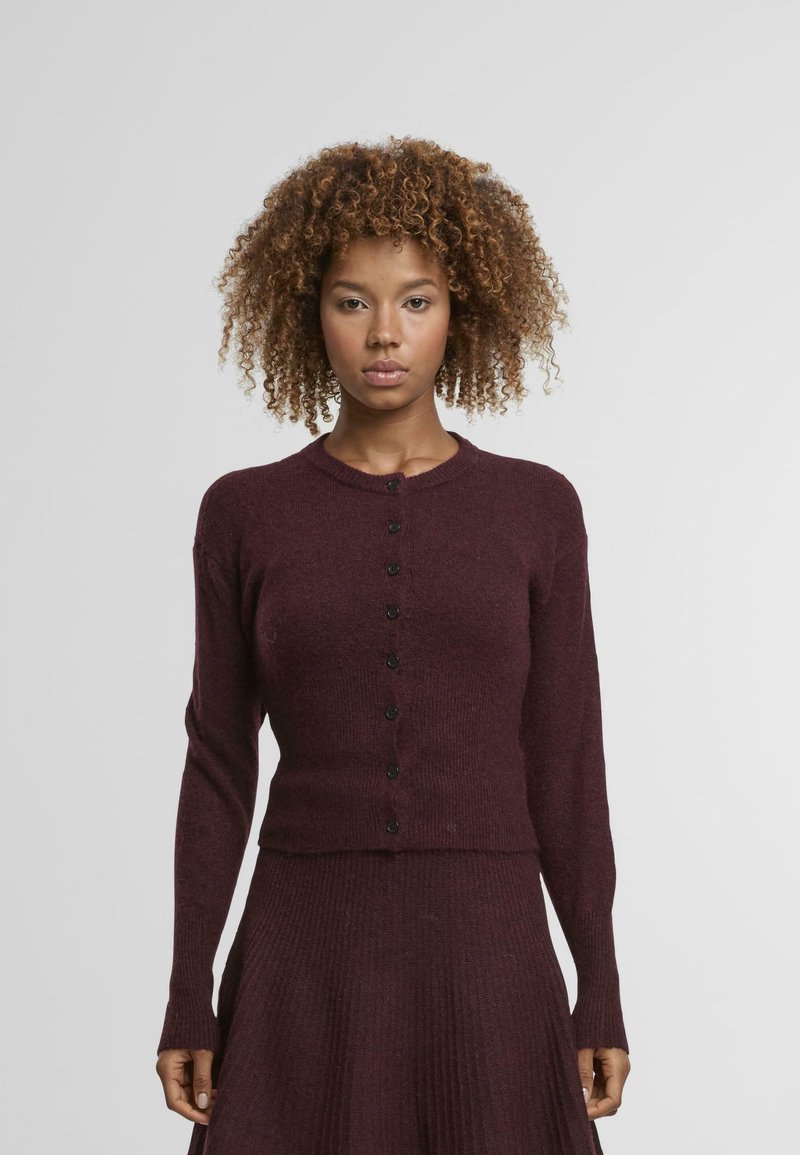 Cardigan en tricot bourgogne avec un col rond, des manches longues et des boutons noirs sur le devant. Tissu texturé avec une finition douce.