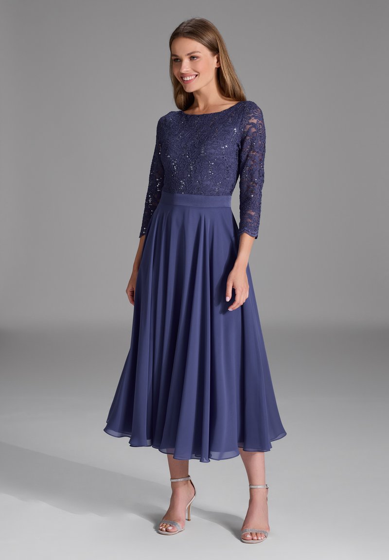 Robe bleu marine avec un corsage en dentelle, des manches trois-quarts et une jupe fluide. Présente des embellissements délicats et une taille ajustée.