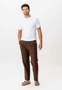 Hvid bomulds T-shirt parret med brune afslappede bukser og beige sandaler. Bukserne har sidelommer og en glat tekstur.