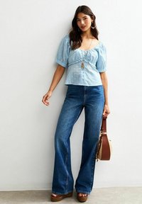 Ljusblå blus med puffärmar och prickar, ihopparad med vida mörkblå jeans och bruna platåsandaler. Accessoriserad med en handväska.