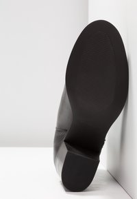 Scarpa in pelle nera con una texture liscia. La suola è piatta, realizzata in gomma con un motivo rigato per una migliore aderenza. La vista laterale mostra una leggera curvatura.