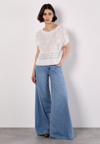White broderie anglaise top with short sleeves, featuring floral patterns and a scalloped hem; paired with light blue wide-leg denim jeans.