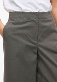 Pilkos kelnės iš glotnios medžiagos, su siaura juosmens dalimi, subtiliomis priekinėmis klostėmis ir šoninėmis kišenėmis, pasižyminčios švariu, moderniu dizainu.