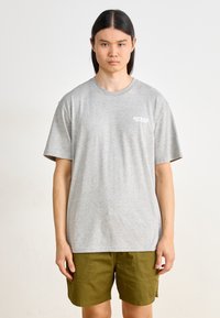 Gray short-sleeve t-shirt made of cotton with a round neckline. Features a small white logo on the left chest. Styled with olive green shorts.