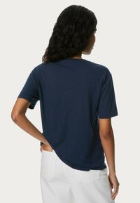 Marinblå t-shirt med korta ärmar och avslappnad passform, med rundad halsringning och mjukt, texturerat tyg. Baksidan visar kantdetalj.