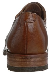 Chaussure en cuir marron avec une texture lisse, talon arrondi et semelle en bois. Détails de couture visibles à l'arrière, design minimaliste.