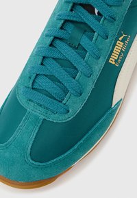 Κοντινό πλάνο του αθλητικού παπουτσιού Puma Easy Rider σε τυρκουάζ, με υφές από σουέντ και ύφασμα, τυρκουάζ κορδόνια και μπεζ ενδιάμεση σόλα.