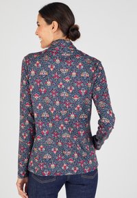 Maglietta a maniche lunghe in tessuto blu navy con intricati motivi floreali in rosa, crema e blu. Design con colletto alto e silhouette aderente.