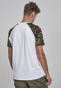 White cotton t-shirt with camouflage raglan sleeves, featuring a crew neck and a standard fit, smooth texture, and no visible logos or patterns.