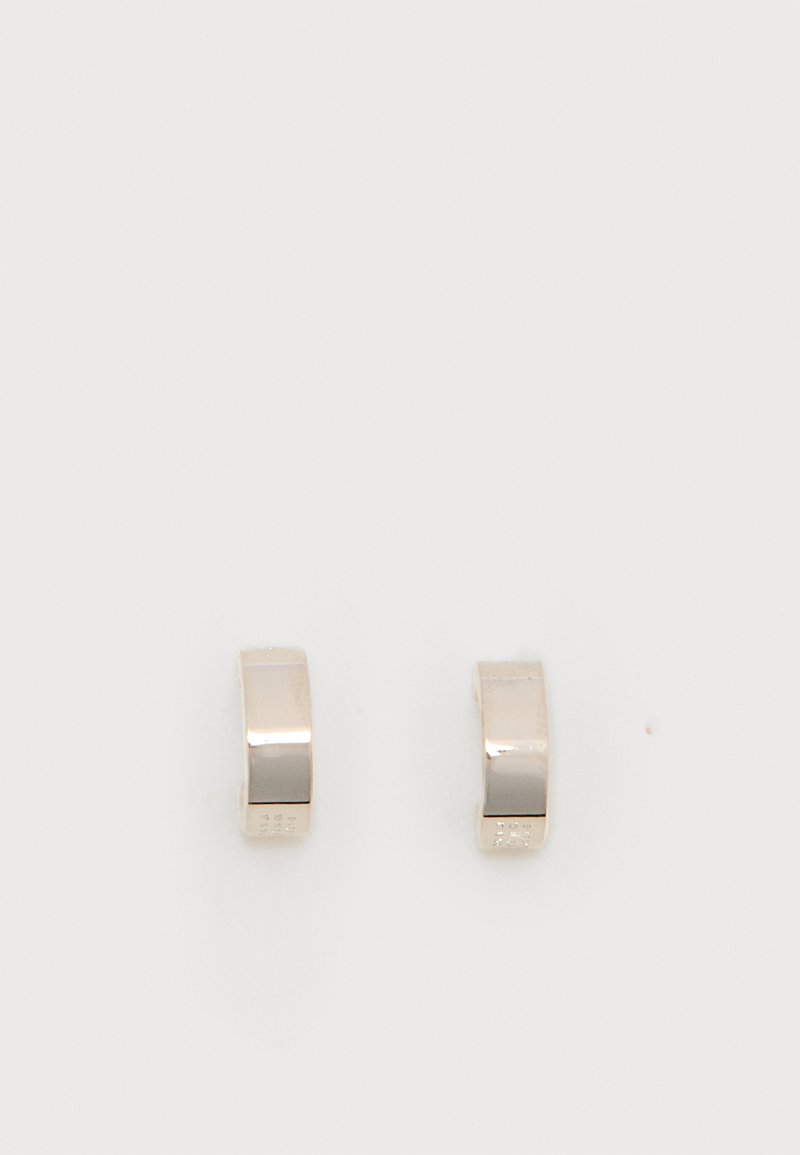 Ζεύγος μικρών, γυαλιστερών ασημένιων κρίκων με λείες, καμπυλωτές επιφάνειες σε απλό λευκό φόντο.