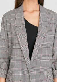 Blazer à carreaux gris avec accents noirs, revers crantés et manches trois-quarts. Présente un motif à carreaux de différentes nuances.
