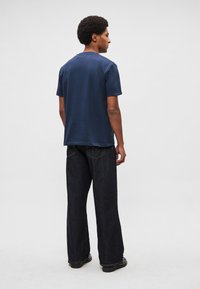 Tumši zila kokvilnas t-krekls ar apaļu apkakli, īsām piedurknēm un vaļēju piegriezumu, kombinēts ar tumšām platajiem džinsa biksēm un melniem apaviem.