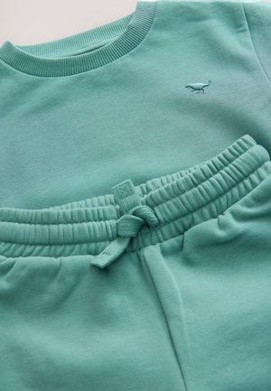 Set di felpa e pantaloni color turchese chiaro realizzato in tessuto morbido. La felpa presenta una scollatura a costine; i pantaloni hanno una vita elastica con coulisse.