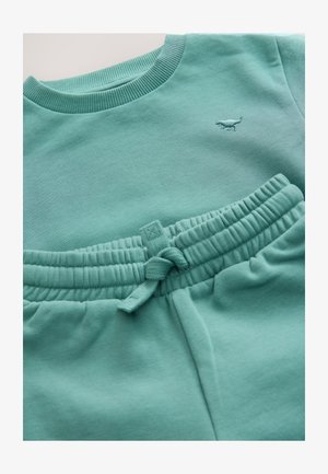 Heleroheline sinakashall dressipluus ja pükside komplekt, valmistatud pehmest kangast. Dressipluusi kaelus on soonikuga; pükstel on elastne vöökoht ning paelad.