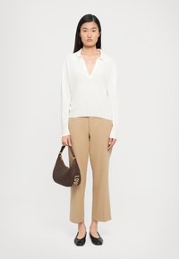 Weißer Pullover mit langem Arm und V-Ausschnitt, beige Schlaghose, schwarze Ballerinas und eine braune Schultertasche mit goldener "LOVE"-Prägung.
