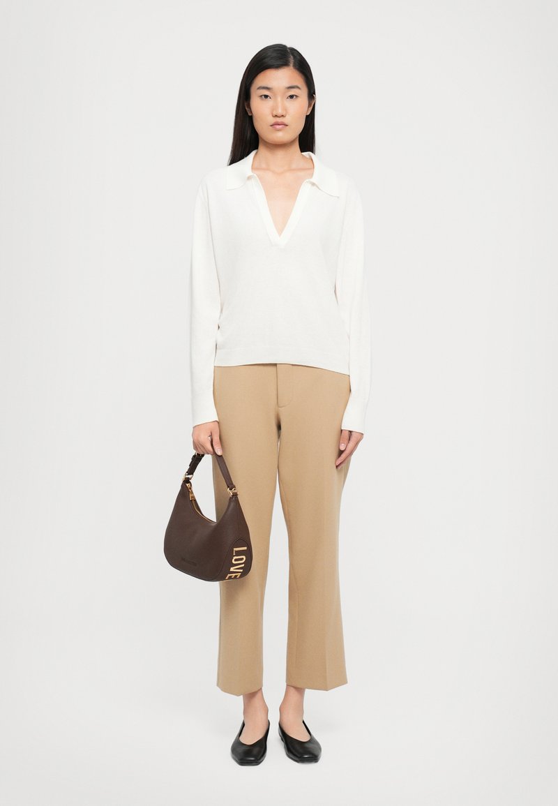 Weißer Pullover mit langem Arm und V-Ausschnitt, beige Schlaghose, schwarze Ballerinas und eine braune Schultertasche mit goldener "LOVE"-Prägung.