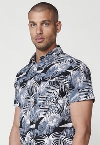 Camicia nera a maniche corte con bottoni, decorata con una stampa floreale tropicale in bianco e blu, dotata di colletto a punta e di una piccola etichetta con logo sul petto.