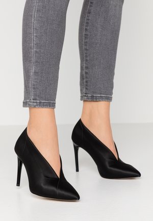 Czarne szpilki z wyciągniętym czubkiem i v-kształtnym wzorem, o gładkim satynowym wykończeniu i obcasie w stylu stiletto.