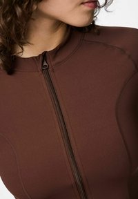 Ruda naršymo apranga su aukštu apykakliu ir užtrauktuku priekyje, pagaminta iš lygaus, tempiančio audinio, siūta plokščiomis siūlėmis patogumui užtikrinti.