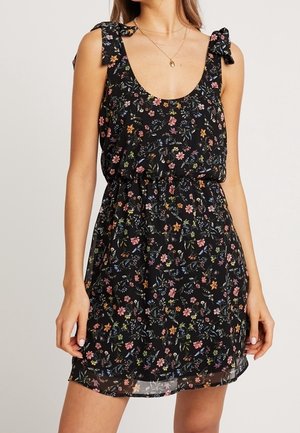 Robe noire à fleurs avec un décolleté en scoop, des bretelles nouées et une taille élastique. Comprend de petites fleurs colorées et un tissu léger et fluide.
