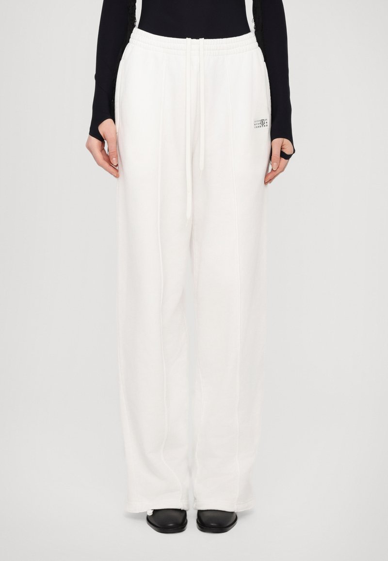White sweatpants with a relaxed fit, elastic waistband, drawstring detail, and logo accent, made from soft fabric.