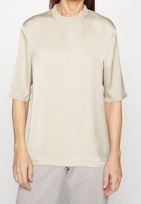 Kortærmet, beige top med høj halsudskæring. Fremstillet af glat, blankt stof. Enkel design med oprullede ærmer og en afslappet pasform.