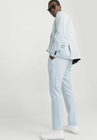Chaqueta y pantalones de traje azul claro, hechos de una tela suave, combinados con zapatillas blancas. Presenta botones negros y un sutil patrón texturizado.