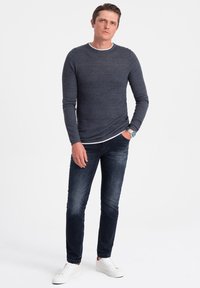 Dunkelblaues Langarmhemd mit einem weißen Kragen, kombiniert mit dunklen Jeans und weißen Sneakern. Glatte Textur, figurbetonte Passform.