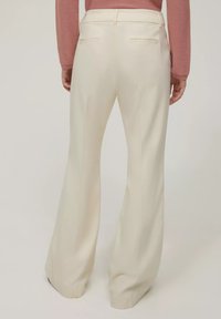 Pantaloni a zampa d'elefante beige con una texture morbida, dotati di due tasche posteriori e una vita sagomata. Adatti per un look smart casual.