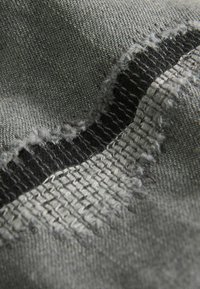 Sivý textil má rôzne tkaniny a zúbkované čierne vyšívanie, s textúrovaným povrchom a rozstrapkanými okrajmi pre väčší vizuálny záujem.