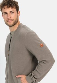 Lichtbruine cardigan met rits, voorzien van een gestructureerd breisel, ribgebreide kraag en manchetten, en een leren logo-opdruk op de linkermouw.