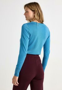 Maglione a maniche lunghe blu a maglia con scollatura rotonda, maniche attillate e una superficie liscia, abbinato a pantaloni bordeaux a vita alta.