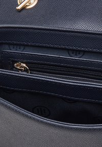 Interno di borsa a tracolla blu navy con texture, dotato di una tasca con zip, due scomparti aperti e fodera con motivo logo. Accenti in oro.