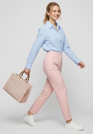 Jeune femme marchant, portant une chemise à carreaux bleu clair, un pantalon rose, des baskets blanches, et portant un sac à main rose clair avec des poignées en bambou.