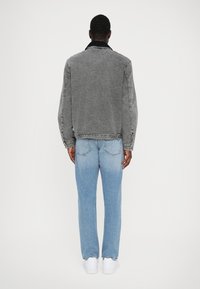 Veste en denim gris avec un col noir, associée à un jean en denim bleu clair. Le tissu semble texturé avec une coupe décontractée et des coutures visibles.