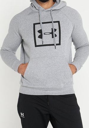 Sweat à capuche gris avec un grand logo Under Armour noir dans un carré. Comprend une poche avant, une capuche avec cordon de serrage et des poignets côtelés.