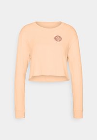 Light peach long-sleeve crop top made of soft fabric, featuring a round neckline and a small, circular Nike logo on the left chest.