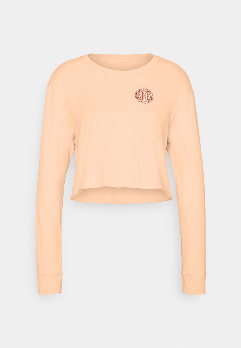 Light peach long-sleeve crop top made of soft fabric, featuring a round neckline and a small, circular Nike logo on the left chest.
