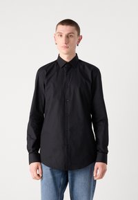 Svart langermet skjorte laget av lett stoff, med knapper foran, spiss krage og standard mansjetter, kombinert med blå jeans.