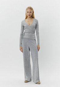 Grauer Wickeltop mit langen Ärmeln, kombiniert mit weiten grauen Hosen, beide aus einem weichen, strukturierten Stoff. Das Ensemble verfügt über ein tiefes V-Ausschnitt-Design.