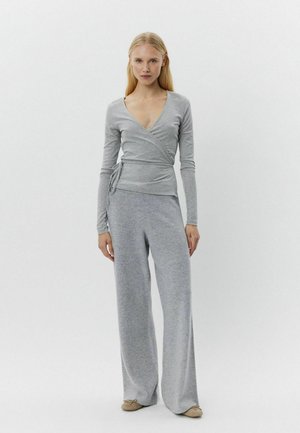 Szürke, hosszú ujjú, átkötős felső, széles szárú szürke nadrággal párosítva, mindkettő puha, texturált anyagból készült. Az összeállítás mély V-nyakú dizájnnal rendelkezik.