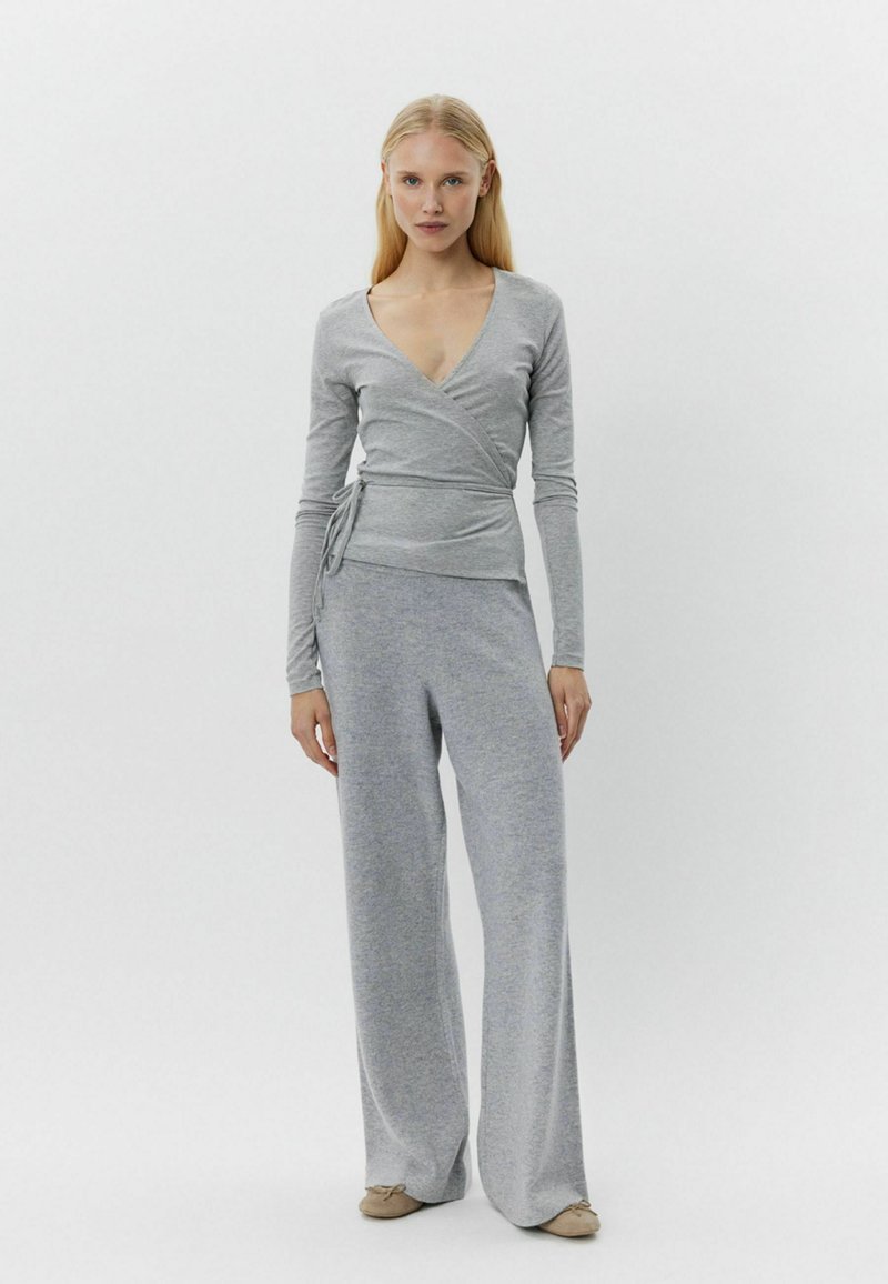 Grauer Wickeltop mit langen Ärmeln, kombiniert mit weiten grauen Hosen, beide aus einem weichen, strukturierten Stoff. Das Ensemble verfügt über ein tiefes V-Ausschnitt-Design.
