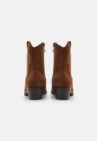Bottines en daim marron avec une finition texturée, dotées d'une fermeture éclair et de coutures décoratives sur le talon. Design à talon bloc.