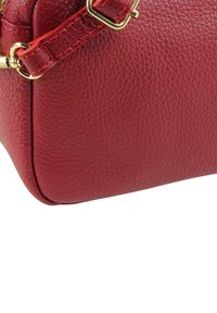 Rote Lederhandtasche mit Struktur, goldfarbenem Reißverschluss und Beschlägen. Runde Form mit strukturiertem Boden. Verstellbarer Riemen.