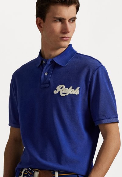 Tricou polo albastru dintr-un material texturat, cu o clapetă cu trei nasturi și un logo brodat "Ralph" în alb. Mâneci scurte.