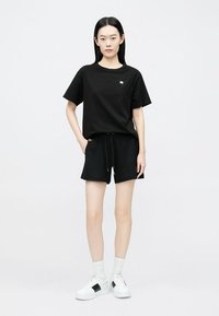 Zwart katoenen T-shirt met een ronde hals en korte mouwen, gecombineerd met zwarte short met trekkoord. Witte sneakers met zwarte accenten.