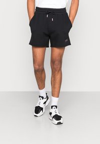 Shorts de algodón negros con cintura elástica y cordón, con bolsillos laterales y un pequeño detalle del logotipo rosa. Combinados con zapatillas negras y blancas.