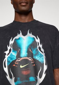 Čierne grafické tričko s živou modrou a červenou potlačou, so striebornými akcentmi pripomínajúcimi plameň a centrálnym logom Nike.