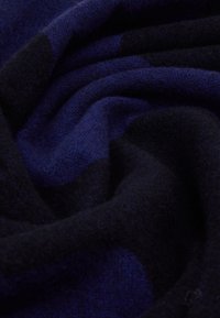 Tissu doux plié avec un motif à carreaux bleu foncé et noir, montrant la texture et des courbes douces.